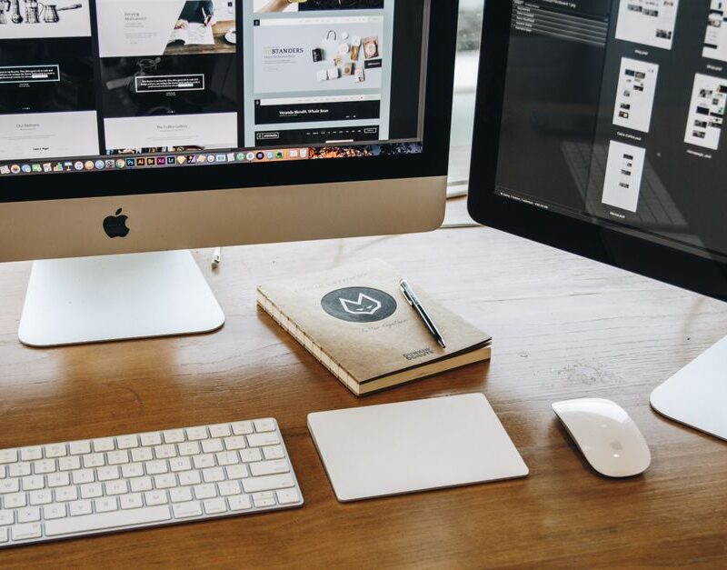 Web design pro — A minimalist desk setup featuring dual monitors, keyboard, mouse, and notebook for productivity.