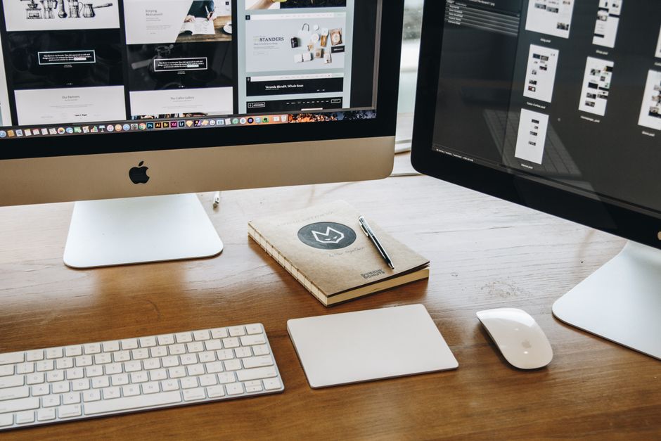Web design pro — A minimalist desk setup featuring dual monitors, keyboard, mouse, and notebook for productivity.